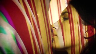 Ellie Luna and Leona Mia kiss slowly under swirling red and yellow light projections